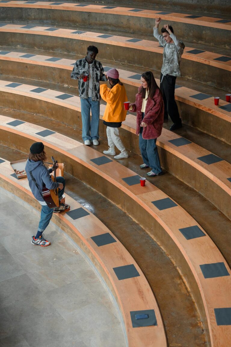 Diverse group of young adults dancing and bonding with acoustic guitar music in an amphitheater.
