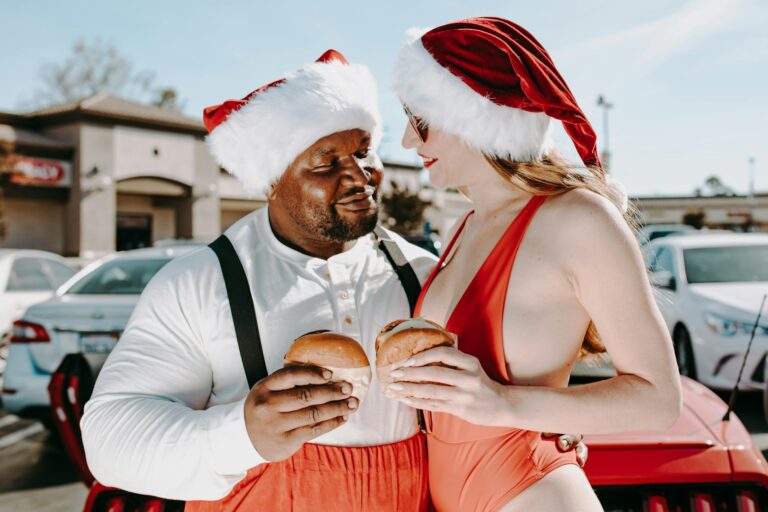 Festive couple in Santa hats enjoying burgers, showcasing holiday fun.